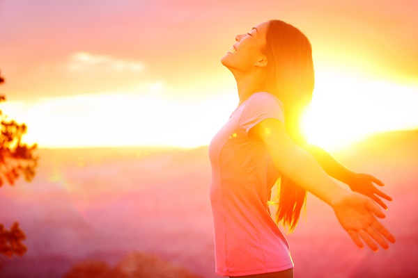 Woman in front of a sunrise holding her arms out